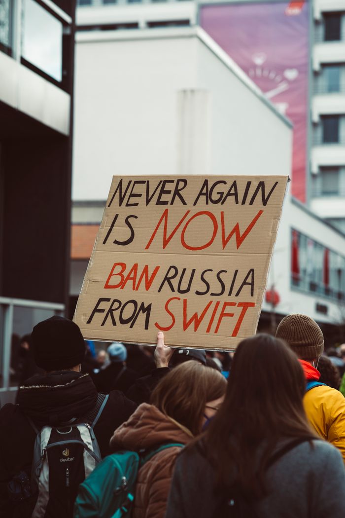 Crowd at protest with sign 'Ban Russia from SWIFT' emphasizing activism and collective voice.
