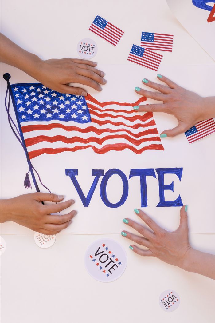 Services Hands arranging a patriotic voting poster with American flags, encouraging civic participation.